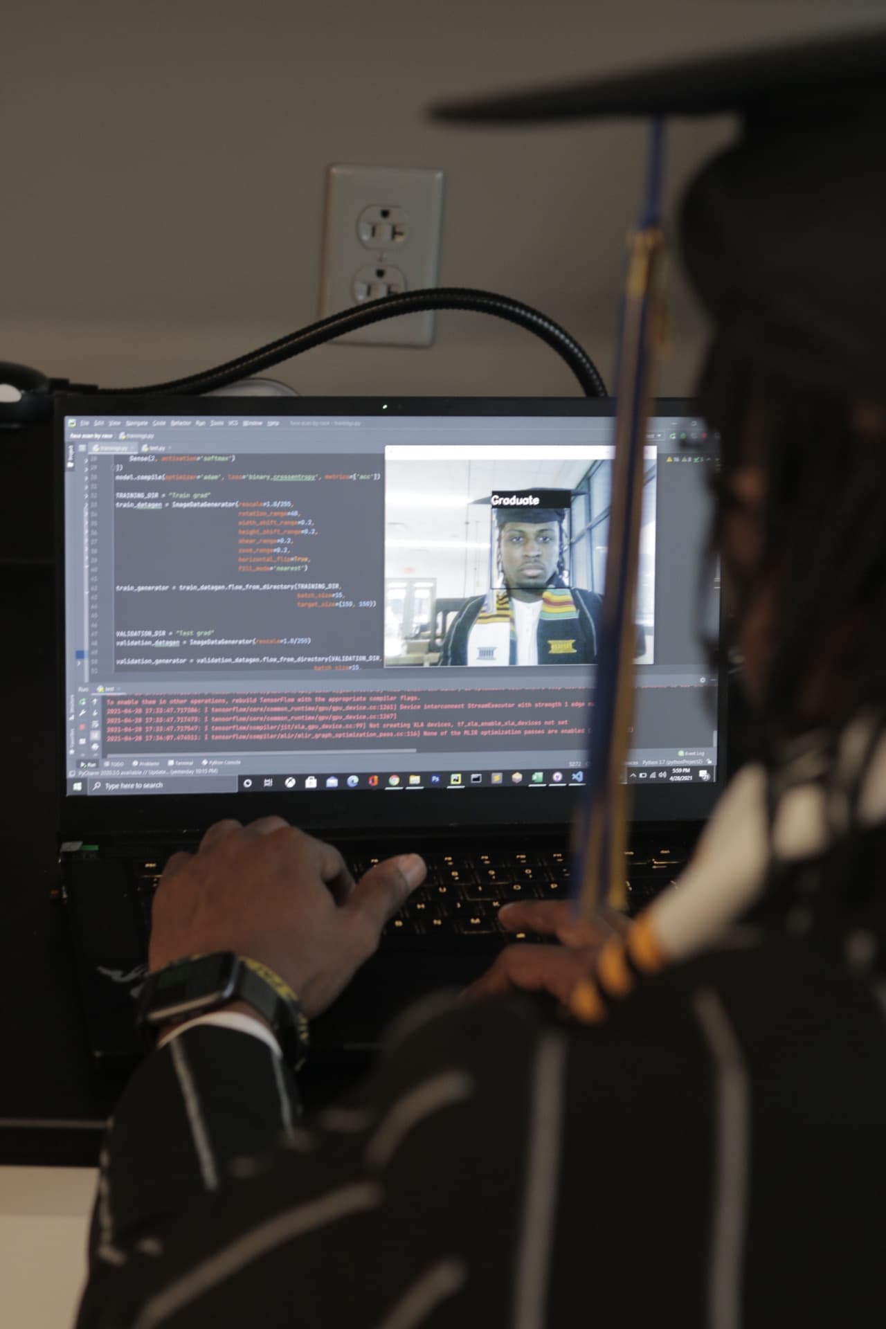 Jordan in graduation attire working at a laptop displaying code and a computer vision project